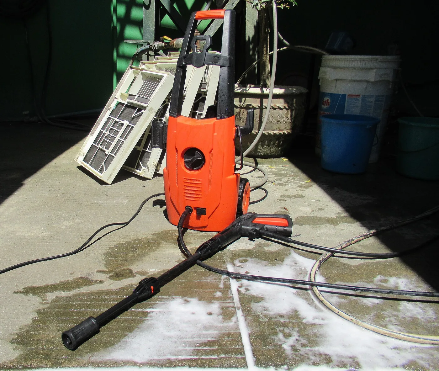 Nettoyeur haute pression électrique avec son pistolet et sa lance sur un sol mouillé