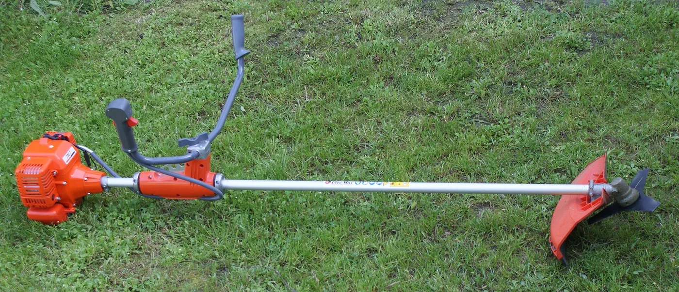 Débroussailleuse thermique à moteur 2 temps et guidon posée dans l'herbe