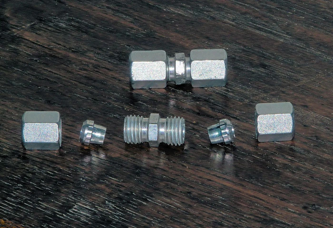 Raccord hydraulique à bague coupante démonté : corps fileté, écrous et bagues