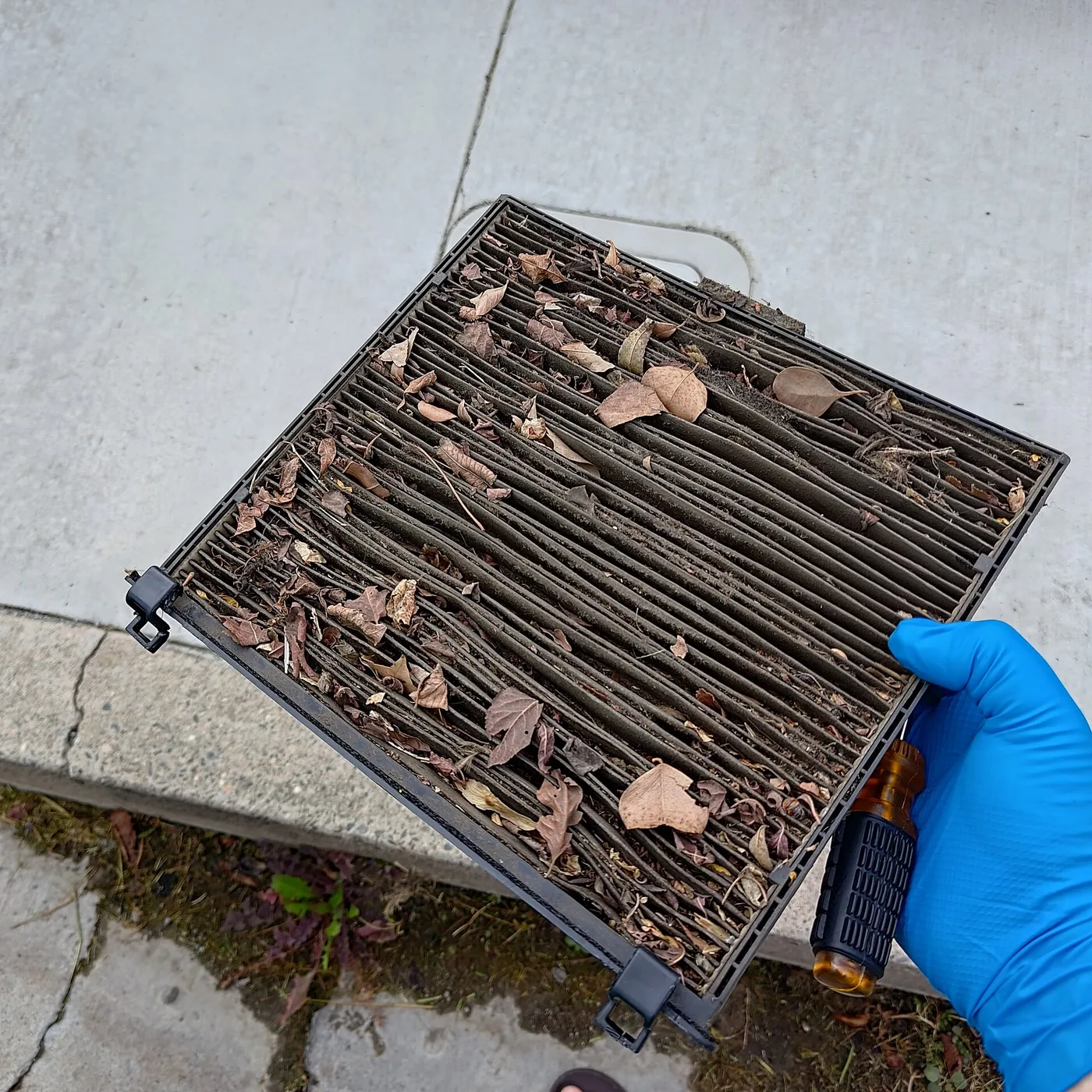 Filtre d'habitacle plissé encrassé de feuilles et de poussière, tenu à la main gantée