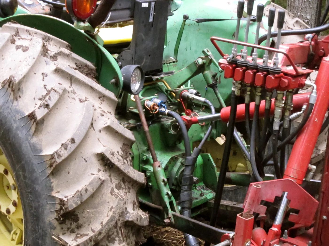 Distributeur hydraulique à leviers et flexibles raccordés à l'arrière d'un tracteur couvert de boue