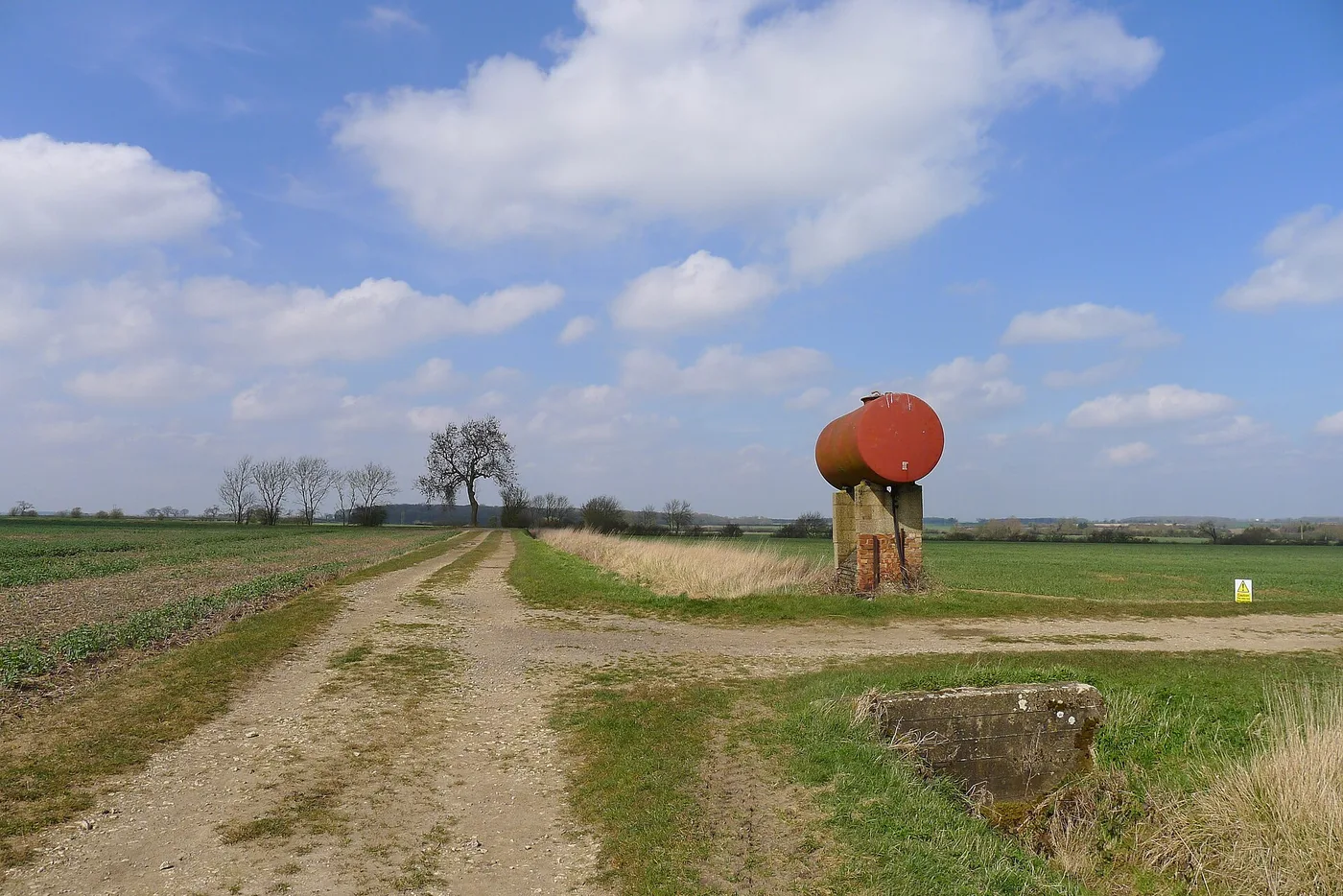 Cuve de carburant aérienne en acier posée sur un socle en briques, au croisement de chemins d'exploitation